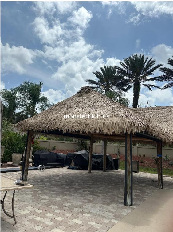 Tiki hut on stone pavers with palm trees and outdoor furniture